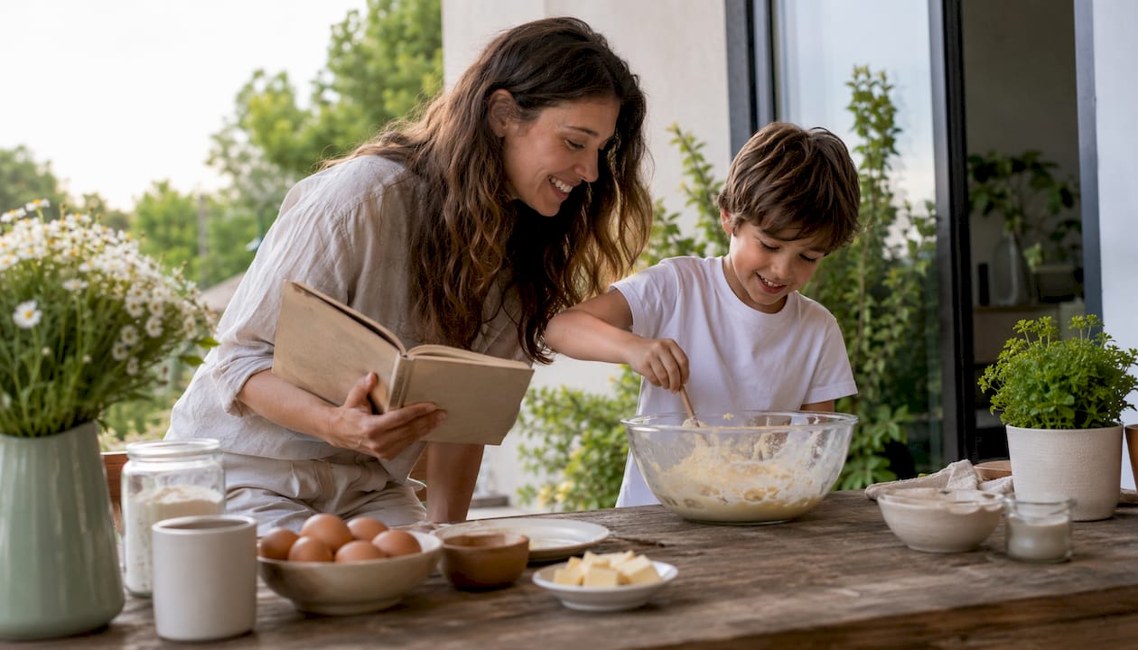 Mãe e filho a confecionar juntos o bolo da comunhão na cozinha lá de casa, moderna e cheia de luz.