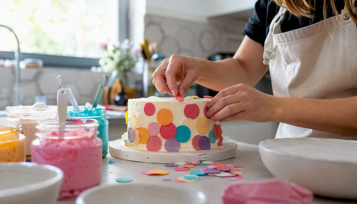Unas manos decoran un pastel con adornos comestibles de colores vivos.