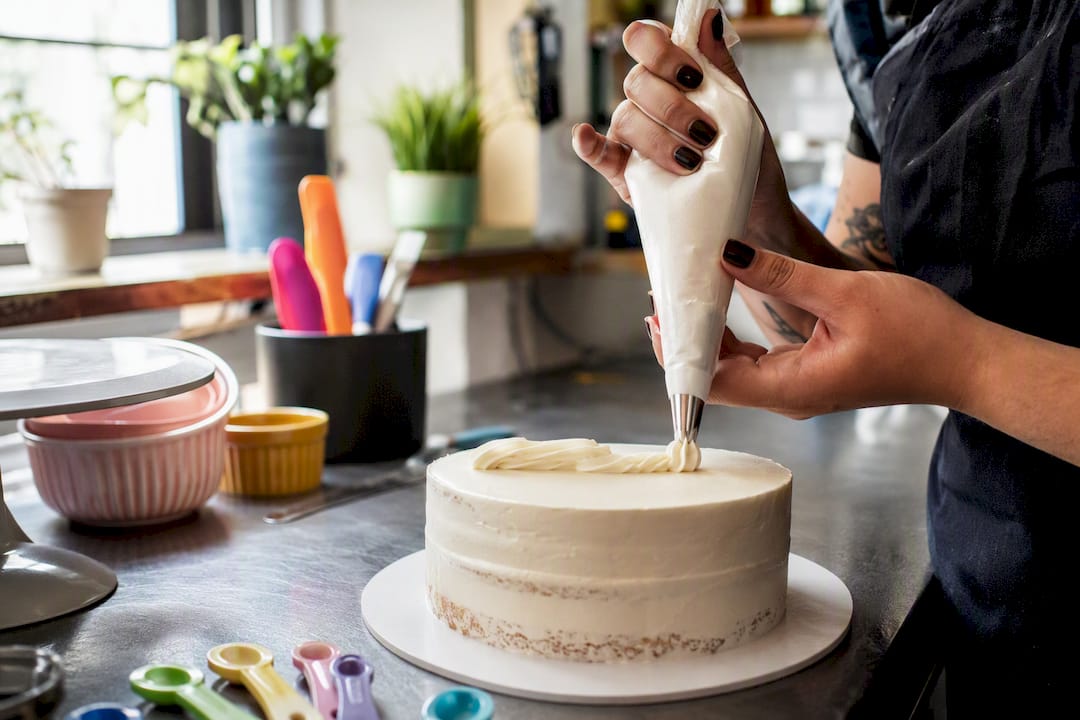 Mãos a decorar um bolo com letras feitas com saco de pasteleiro